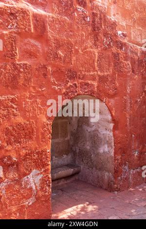 Un mur de briques rouges avec une petite arche. L'arche est en pierre et est légèrement ouverte. Le mur est recouvert d'une texture rugueuse et il est altéré Banque D'Images