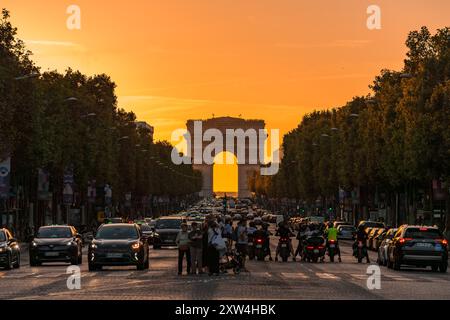 Paris, France - 10 août 2024 : circulation animée et foule au carrefour des champs-Élysées avec Arc de Triomphe au coucher du soleil Banque D'Images