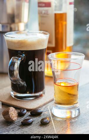 Tasse de café frais et un verre dosé avec whisky pour marquer le café irlandais. À l'avant, les grains de café au chocolat et la muscade. Banque D'Images