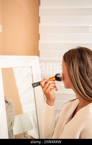 vertical gros plan jeune femme blonde est vu appliquer le rougissement avec un pinceau comme elle regarde dans un miroir. L'image souligne son applicati de maquillage personnel Banque D'Images