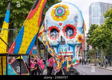 Belfast Mela Carnival Parade - crâne humain vif lumineux jour du flotteur mort multicolore au point de rassemblement. Belfast, Royaume-Uni - 17 août 2024. Banque D'Images