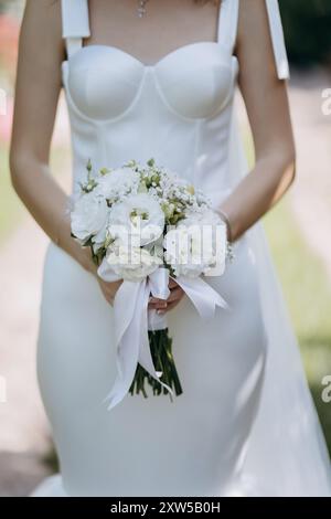 Mariée élégante tenant un bouquet floral blanc dans une robe de mariée minimaliste, symbolisant la pureté Banque D'Images