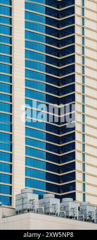 Plusieurs grandes unités de climatisation HVAC et de grands refroidisseurs de chauffage industriels sont installés sur le toit d'un bâtiment avec des fenêtres en verre bleu, mettant en valeur une infrastructure moderne pour le contrôle du climat Banque D'Images