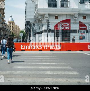 Bakou, Azerbaïdjan - 3 mai 2019 : une élégante femme azérie traverse la rue à Bakou après la course de formule 1, avec la signalisation Emirates Fly Better visible sur les barrières de protection qui bordent la rue, soulignant l'intersection entre style et événements internationaux. Banque D'Images