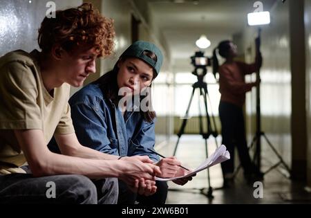 Personnes discutant de la configuration de la scène pendant le tournage en intérieur avec un équipement de caméra en arrière-plan création d'une scène de film dans un environnement professionnel Banque D'Images