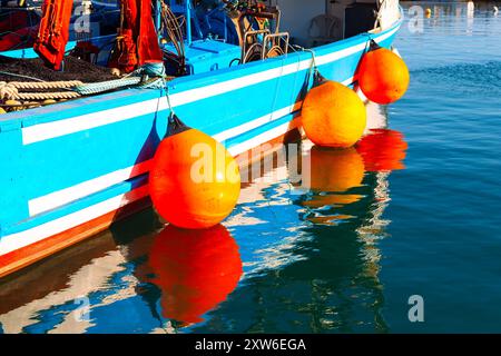Bateau équipé de bouées orange vif, flottant calmement à la surface de l'eau. Bateau de pêche amarré avec garde-boue Banque D'Images