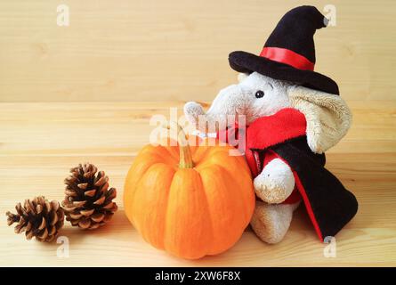 Poupée éléphant mignonne en costume de sorcier avec citrouille mûre et pommes de pin séchées sur fond en bois Banque D'Images