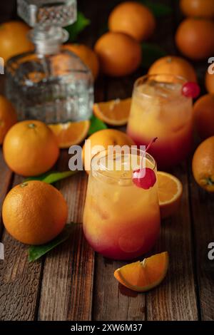 Cocktail tequila Sunrise, superposé de tequila aux teintes vibrantes de jus d'orange et de grenadine, garni d'une cerise maraschino. Banque D'Images