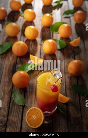 Cocktail tequila Sunrise, superposé de tequila aux teintes vibrantes de jus d'orange et de grenadine, garni d'une brochette de cerises maraschino. Banque D'Images