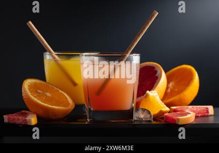 Verres de pamplemousse et jus d'orange avec de la glace sur un fond noir. Boissons rafraîchissantes avec des tranches de fruits. Banque D'Images