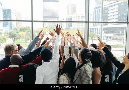 Groupe diversifié de professionnels levant la main ensemble, célébrant le succès et la collaboration dans un environnement de bureau moderne. Banque D'Images