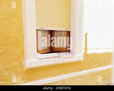 Gros plan horizontal d'une charmante fenêtre italienne avec stores semi-ouverts et mur jaune vif à la lumière du soleil. Olbia, Sardaigne. Banque D'Images