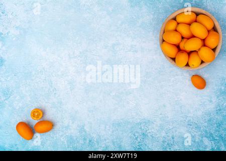 Kumquat dans un bol en bois sur fond bleu. Banque D'Images