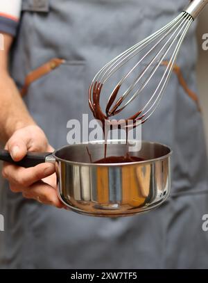 Chef faisant gâteau au chocolat, gros plan des mains tenant un pot. Chocolat fondu au fouet. Banque D'Images