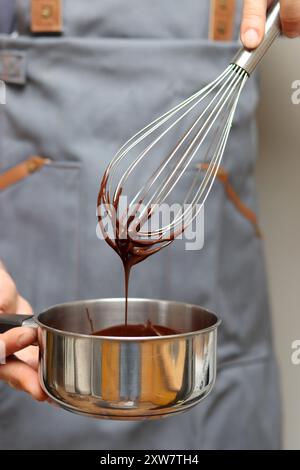 Chef faisant gâteau au chocolat, gros plan des mains tenant un pot. Chocolat fondu au fouet. Banque D'Images