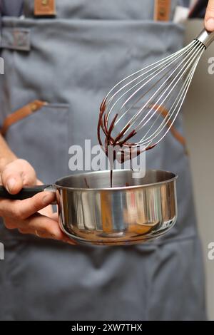 Chef faisant gâteau au chocolat, gros plan des mains tenant un pot. Chocolat fondu au fouet. Banque D'Images