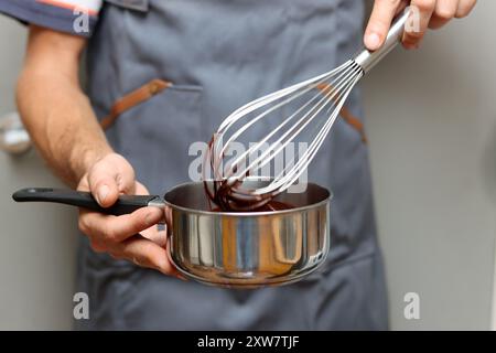 Chef faisant gâteau au chocolat, gros plan des mains tenant un pot. Chocolat fondu au fouet. Banque D'Images