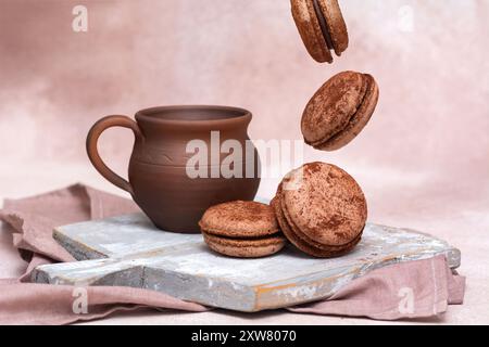 Macarons au chocolat tombant près d'une cruche en argile sur un fond clair Banque D'Images