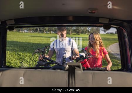 Jeune homme et une femme qui se préparent au vélo tout-terrain, en descendant les vélos de montagne électriques du porte-vélos sur le camping-car. Banque D'Images