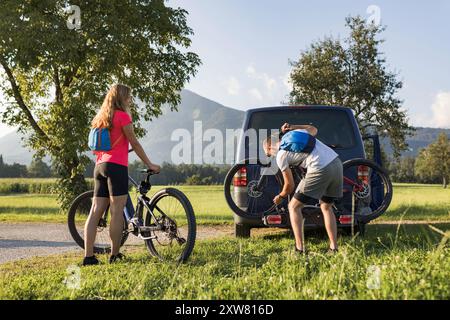 Le jeune homme décharge les vélos de montagne électriques, pour lui et sa petite amie, les soulevant de la galerie d'attelage du véhicule. Banque D'Images