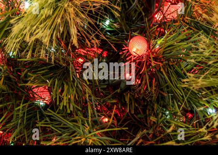 Lumières de Noël rouges éclatantes nichées au milieu d'aiguilles de pin artificielles vertes luxuriantes, créant une ambiance chaleureuse et festive. Prise à Toronto, Canada. Banque D'Images