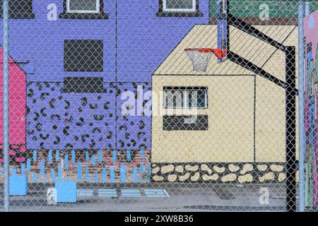 Peinture murale urbaine colorée sur les murs du bâtiment avec un panier de basket-ball et une aire de jeux vue à travers une clôture de maillons de chaîne de fils. Calgary Alberta Canada. Banque D'Images