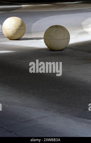 Deux grandes structures sphériques en béton projetant des ombres sur une surface pavée par une journée ensoleillée. Barrière de circulation ronde en béton. Banque D'Images