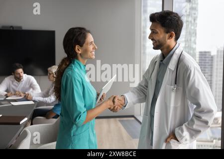 Deux médecins sympathiques et souriants se serrent la main dans la salle de réunion Banque D'Images
