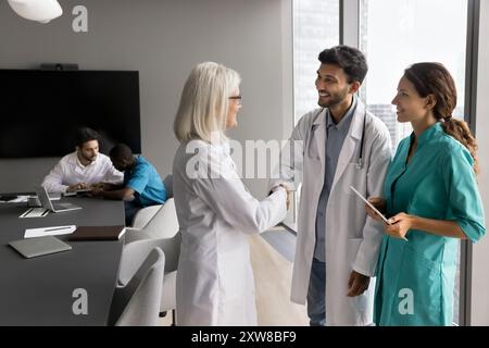 Médecin féminin expérimenté serrant la main avec un médecin masculin plus jeune Banque D'Images