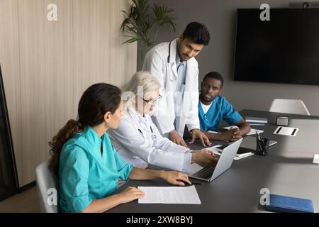 Médecin expérimenté et trois collègues plus jeunes utilisant un ordinateur portable Banque D'Images