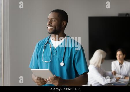 Heureux médecin africain réfléchi, souriant, regardant au loin Banque D'Images
