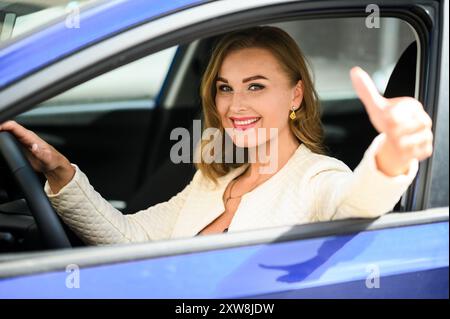 Heureuse femme d'affaires est assise dans sa nouvelle voiture, souriant et donnant un pouce vers le haut, se sentant confiant et satisfait de son achat Banque D'Images