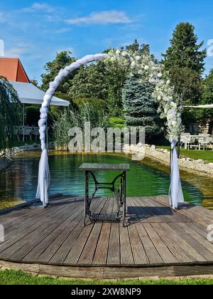 Arche festive décorée de fleurs blanches, construite à côté d'un petit lac de jardin. Herbe vert vif, plantes et arbres. Préparé pour un mariage et un jardin Banque D'Images