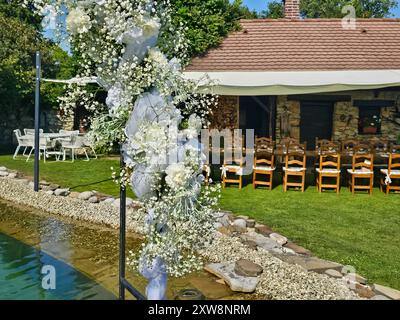 Arche festive décorée de fleurs blanches, construite à côté d'un petit lac de jardin. Herbe vert vif, plantes et arbres. Préparé pour un mariage et un jardin Banque D'Images