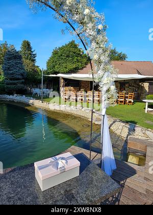 Arche festive avec des fleurs blanches, construite à côté d'un petit lac de jardin. Herbe et arbres vert vif. Préparé pour un mariage et une fête de jardin. Présent sur Banque D'Images