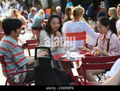 LONDRES, ROYAUME-UNI. 18 août 2024. Trois Chinois jouant une carte chinoise traditionnelle pour aider à une meilleure mémoire au King's Cross Summer Sounds organise une célébration de la culture brésilienne - Olayá à Coal Drops Yard, Londres, Royaume-Uni. ( Credit : Voir Li/Picture Capital/Alamy Live News Banque D'Images