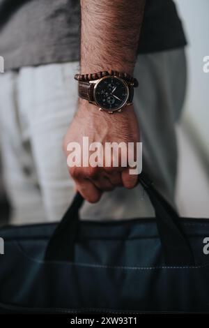 Gros plan d'un homme portant une montre-bracelet et un bracelet, tenant un sac noir Banque D'Images