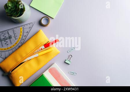 Fournitures scolaires, bloc-notes, étui à crayons jaune, crayon, règle, plante succulente et stylos à pointe feutre sur fond lilas. Vue de dessus, pose à plat, espace de copie. Banque D'Images