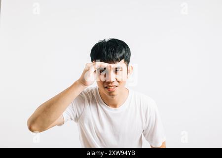 Portrait asiatique souriant jeune homme essayant de voir quelque chose dans la distance tient la paume sur le studio de front Banque D'Images