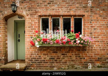 Great Budworth, Cheshire West et Chester, Royaume-Uni - 17 août 2024 - devant un chalet avec une boîte de fenêtre pleine de fleurs et une porte d'entrée verte dans un po Banque D'Images