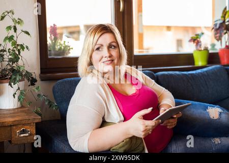 Portrait de belle jeune femme en surpoids à la maison, regardant l'émission de télévision sur tablette, assis dans un fauteuil. Banque D'Images