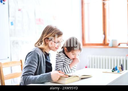 Enseignant travailleur apprenant avec une jeune écolière en classe, aidant avec le problème de lecture. Dyslexie. Leçon individuelle. Banque D'Images