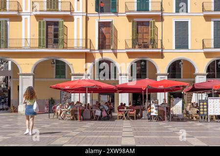 Bâtiment coloré à Palma avec des volets en bois fermés contrastés, donnant sur une place remplie de restaurants en plein air et de parasols rouges vibrants. Banque D'Images