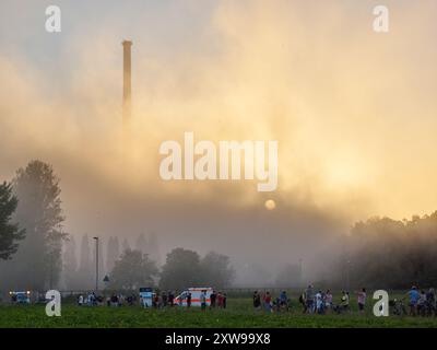 Cheminée, personnes et ambulance en fumée après la démolition de la tour de refroidissement de la centrale nucléaire de Grafenrheinfeld avec le soleil brille à travers la poussière. Grafenrheinfeld, Bavière, Allemagne - 16.08.2024 Banque D'Images