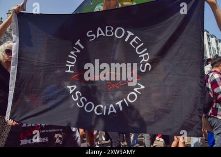 Londres, Royaume-Uni. 18 août 2024. Les militants portent un drapeau de l'association Hunt saboteurs lors de la marche nationale pour les droits des animaux dans le centre de Londres. La manifestation annuelle met en lumière la souffrance et la mort de milliards d'animaux dans tous les domaines de l'activité humaine, lutte pour la libération des animaux et pour la fin de l'exploitation animale, et promeut le véganisme et un mode de vie sans cruauté. Crédit : Vuk Valcic/Alamy Live News Banque D'Images