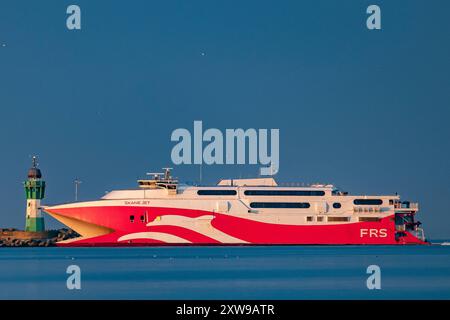 Blick auf die FRS Baltic Faehre und den Leuchtturm am 16.08.2024 im Hafen Mukran in Sassnitz auf der Insel Ruegen. DAS 91 Meter lange Schiff transportiert in der Rekordzeit von 2,5 Stunden Passagiere und Fahrzeuge zwischen Sassnitz, Ruegen, Deutschland, und Trelleborg, Schweden. Die Skane Jet ist eine als Katamaran gebaute Schnellfähre der deutschen Reederei FRS. Skane Jet. Vier kraftvolle Ruston-Motoren, angetrieben von beeindruckenden 40,000 PS, ermoeglichen es diesem Hochgeschwindigkeits-Katamaran, unbeladen eine Spitzengeschwindigkeit von 44 Knoten zu erreichen. Vue sur le FRS Baltic ferr Banque D'Images