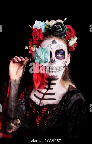 Femme posant avec la rose bleue tout en portant le maquillage squelette et costume d'horreur pour célébrer dios de los muertos pendant Halloween. Dame macabre habillée comme personnage de la Catrina le jour de l'événement mort Banque D'Images