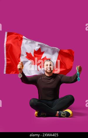 Nageur masculin avec la médaille de la première place assis contre le drapeau canadien sur fond rose Banque D'Images