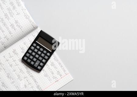 Copybook avec formules mathématiques manuscrites et calculatrice sur fond gris Banque D'Images