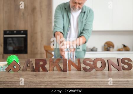 Mot PARKINSON et homme senior prenant un verre D'eau de la table dans la cuisine, gros plan Banque D'Images